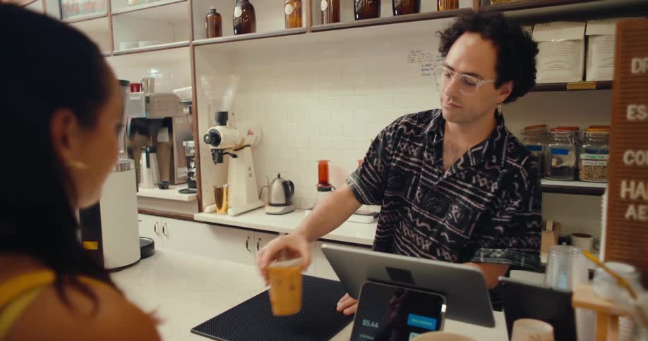 A barista hands a coffee cup to a customer at an indoor coffee shop