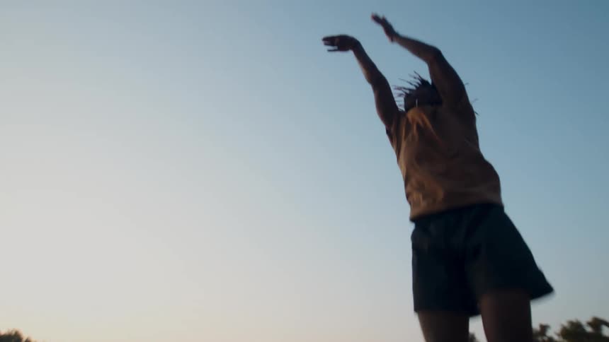 A young man shooting a basketball under a blue sky at evening