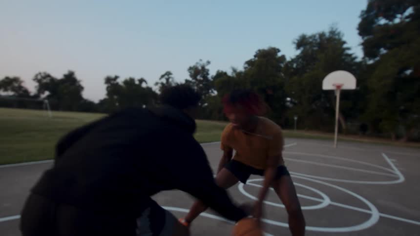 Two young men playing basketball on an open court in the late afternoon