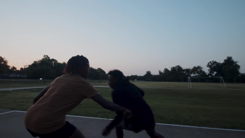 A couple of friends are engaged in a competitive game of basketball on a court at sunset