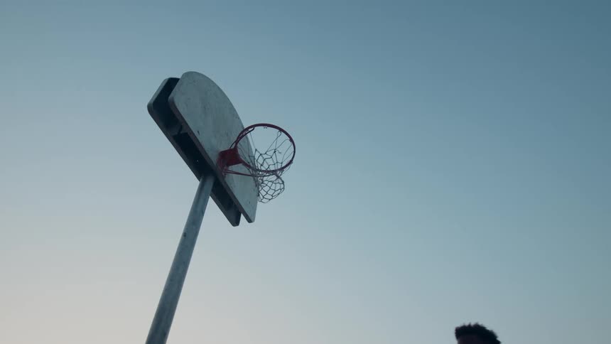 People throwing a basketball into a hoop at evening