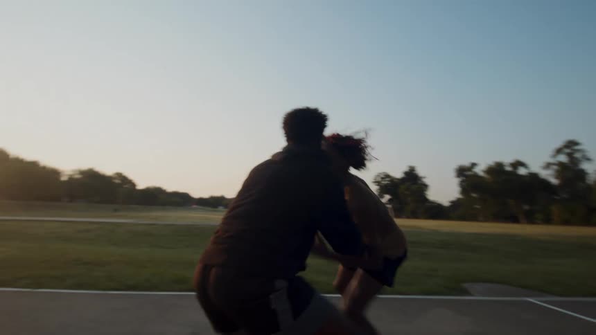 A couple of friends are engaged in a competitive game of basketball on a court at sunset
