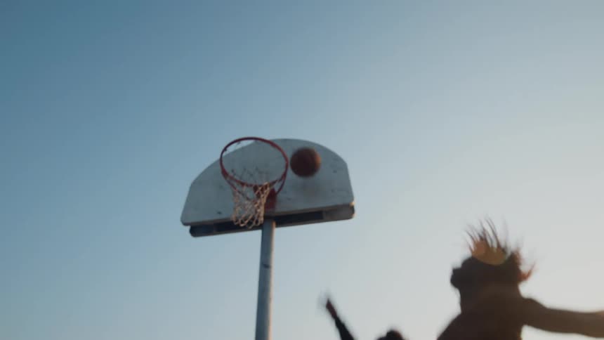 Two young men playing basketball one on one in a park and one of them scores