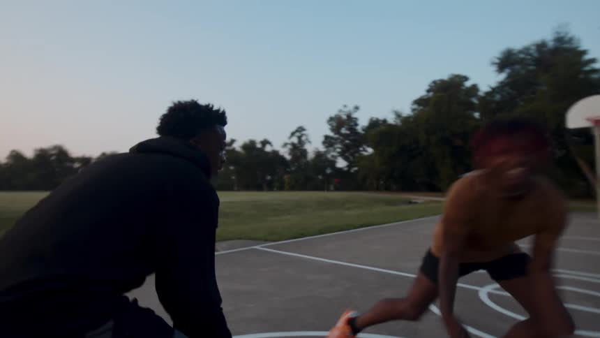 Two young men on a court playing basketball with one of them making a shot