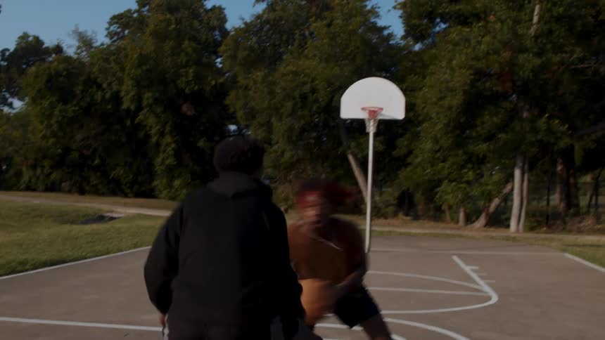 Basketball players play one on one on a court in the park on a sunny day