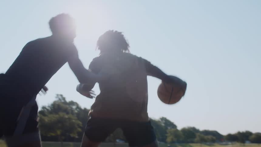 Two teenage boys playing basketball on a court during the day