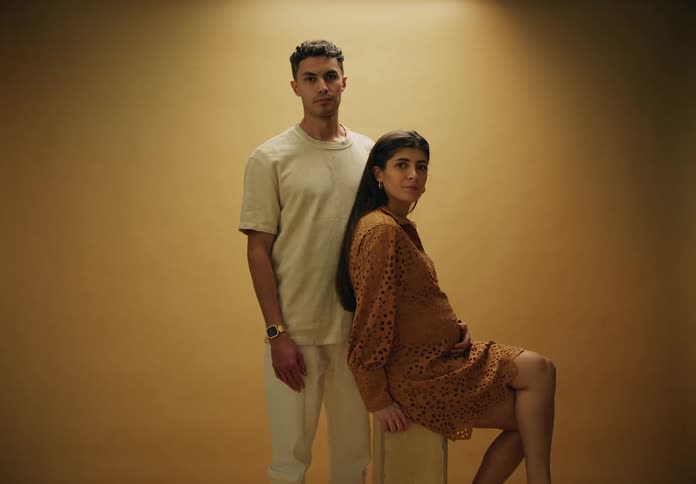 Man standing next to a seated pregnant woman in a dress posing in a studio