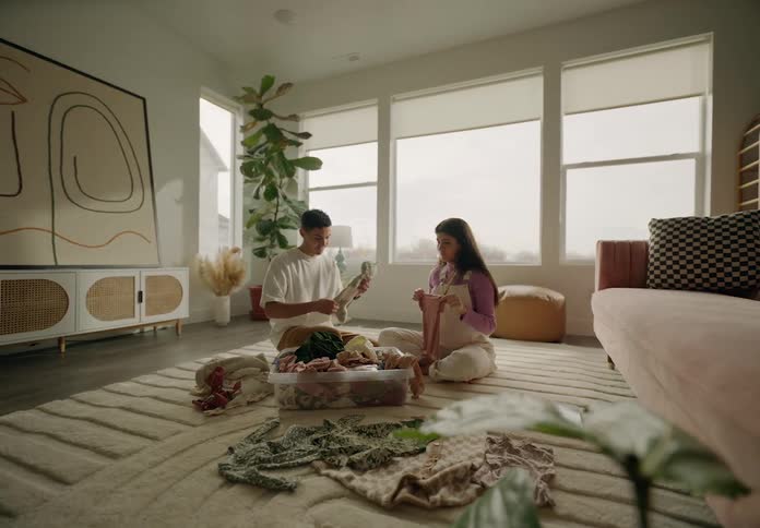 Couple in living room sitting on carpet looking at baby clothes in a box