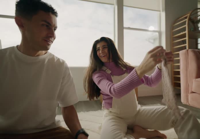 Couple sitting on a living room rug looking at baby clothes