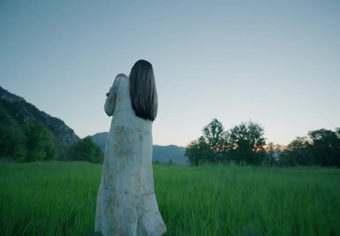Mother carries her baby across a field towards the mountain passing a clothesline on the way