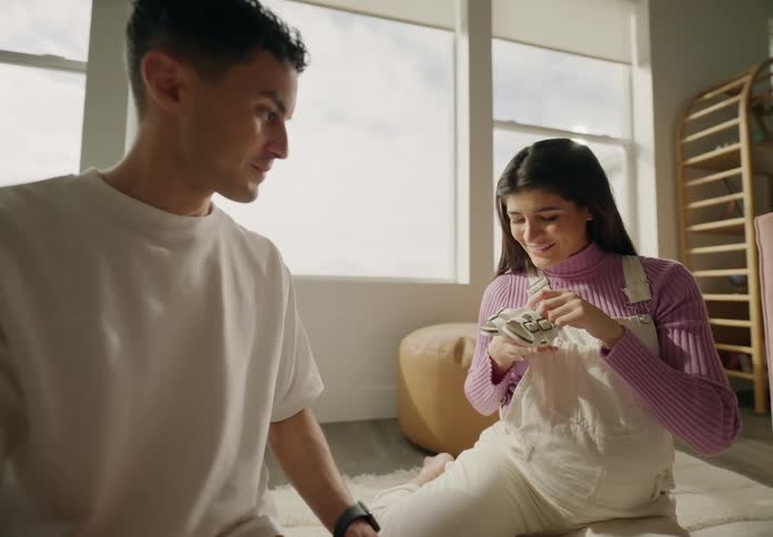 Couple sitting on the living room carpet looking at clothes and a small baby shoe and they both kiss