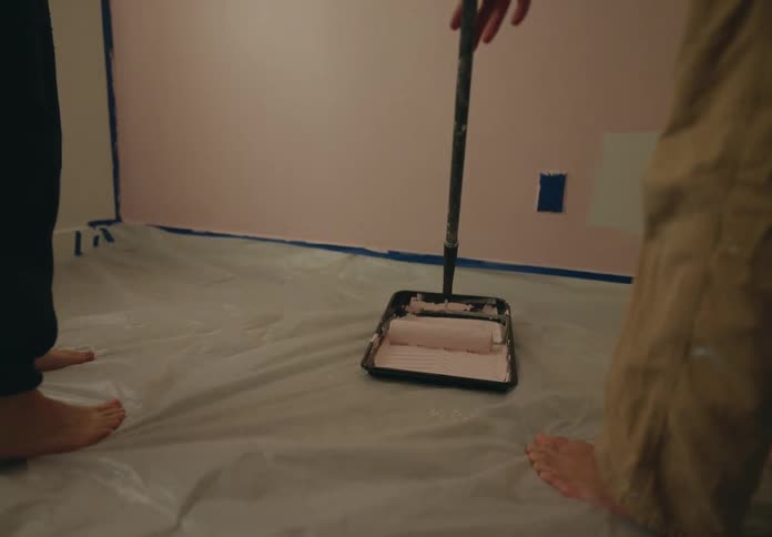 Person with a paint roller being rolled in pink paint inside a room
