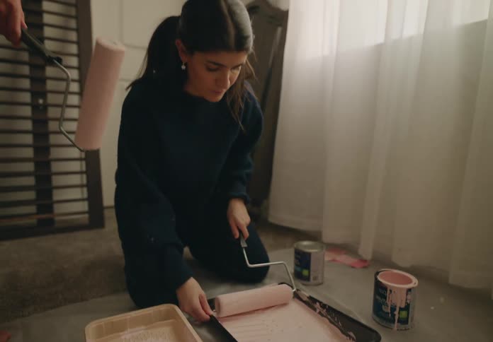 A man and woman are using paint rollers at home