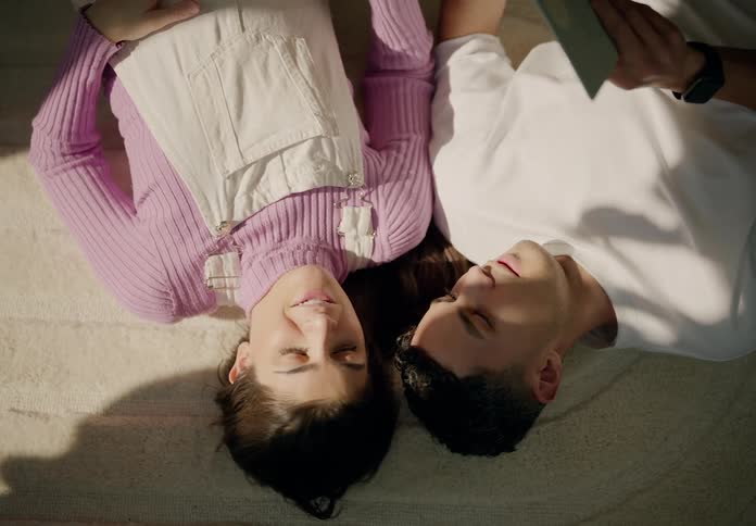 Man and woman lying on a rug reading a book and looking at each other lovingly and happily