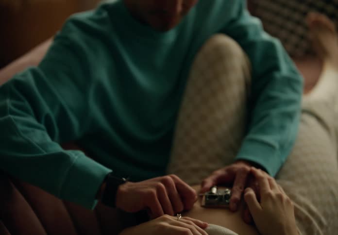 A man laughs while he spins a tiny music box on his girlfriends stomach