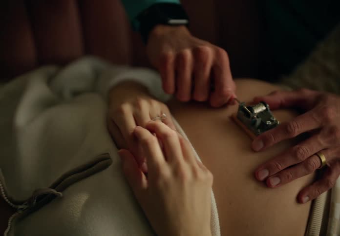 Mans hand turning a crank on the belly of a lying pregnant woman