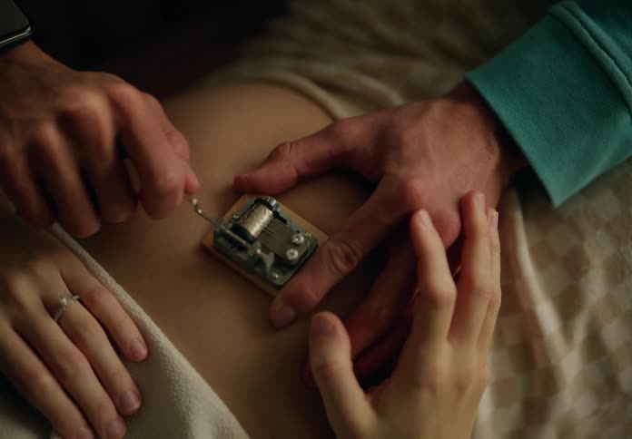 A pregnant woman lying down with a man playing a small music box on her belly