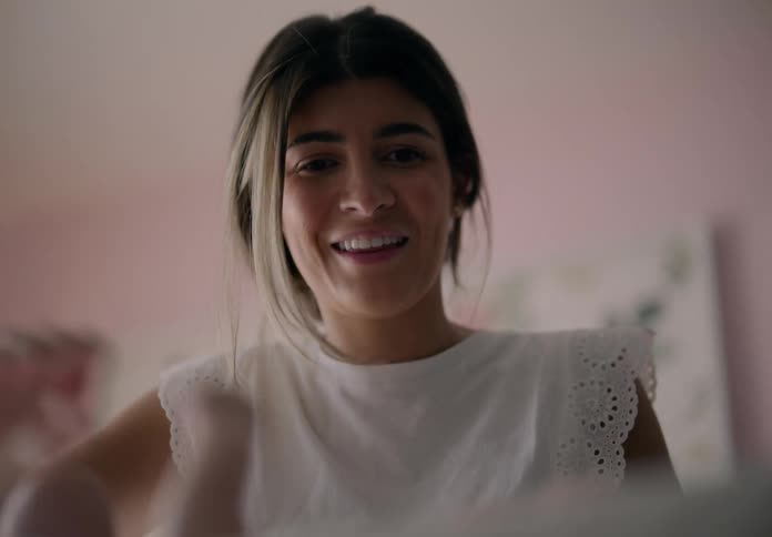 A young woman is happy and smiling as she is changing the clothes of a baby who is in front of her
