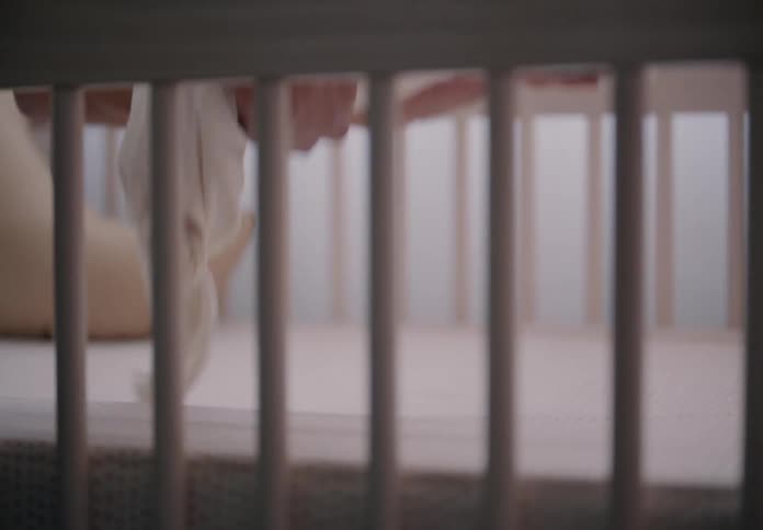 Hands of an adult holding a sleeping baby in the crib