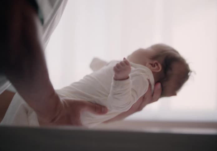 Close up of a father placing a baby on a crib at home