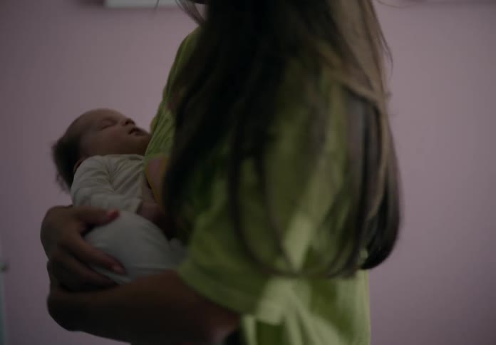 A mother in a bedroom gently rocking and soothing a baby