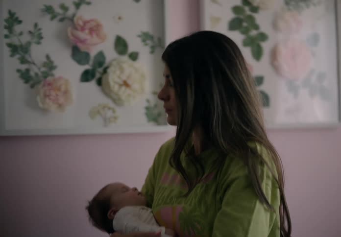 A woman is walking back and forth while she has her child sleeping on her lap and she is moving