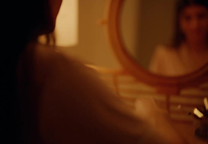 Woman sitting in front of a small round mirror taking capsules from a transparent jar