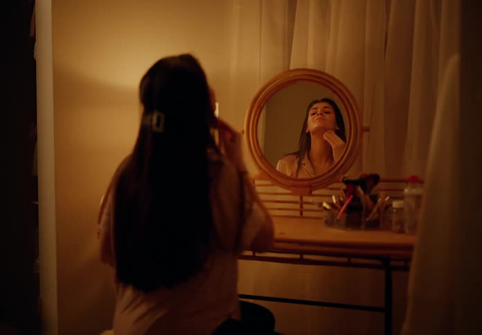 Woman takes off makeup in front of the mirror of a bedside table