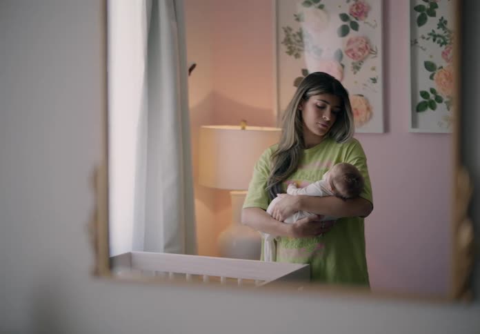 A mother holding a baby their reflection visible in a mirror on a softly lit room