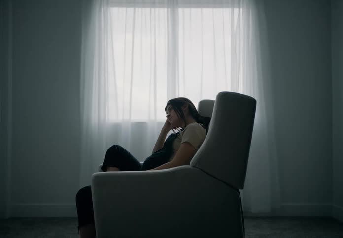 A pregnant woman sitting in a chair by a window with sheer curtains