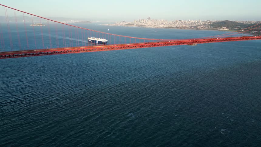 A huge orange bridge that passes over a large amount of water where there is a huge boat that will pass under it