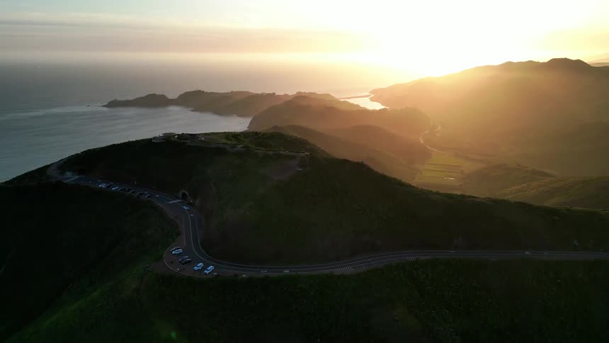 An aerial view captures a scenic coastal mountainous landscape at sunset