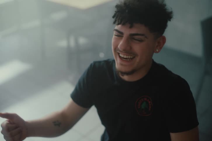 A young man is talking to someone in front of him and is laughing