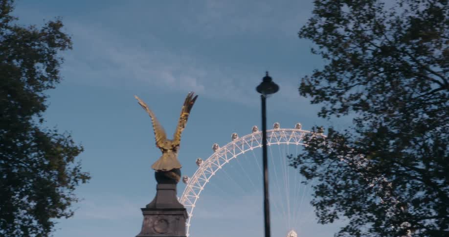 A golden statue with outstretched wings and a large ferris wheel in the background against a blue sky with scattered clouds