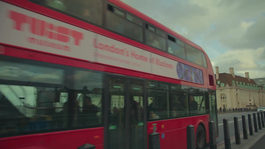 A red bus passing on an asphalt street and behind it there is a beige building
