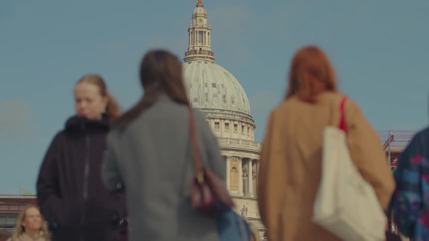 Dome of st pauls cathedral in london standing out against a blue sky and people walking