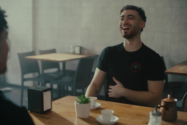 Two male customers in a cafe laugh and play around together
