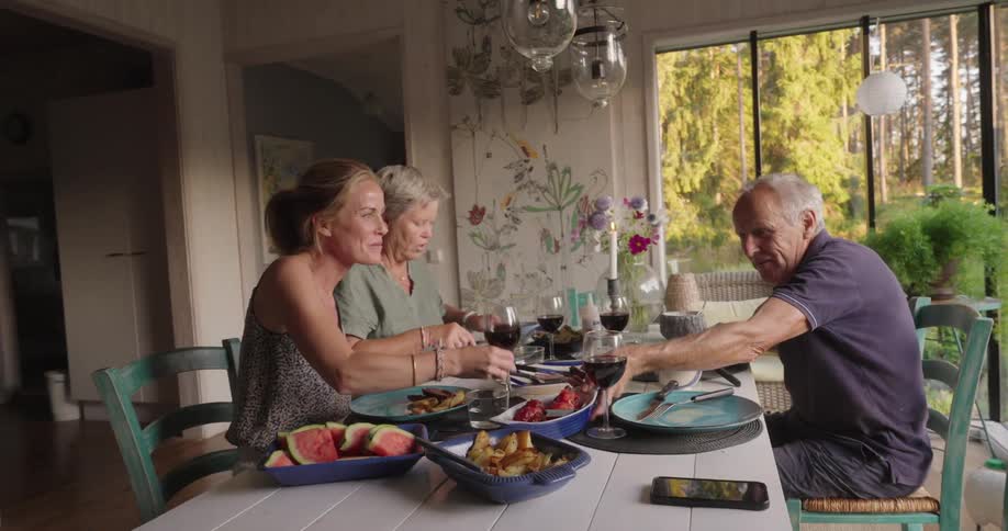 Three people are sitting around a table and are happy while eating and drinking