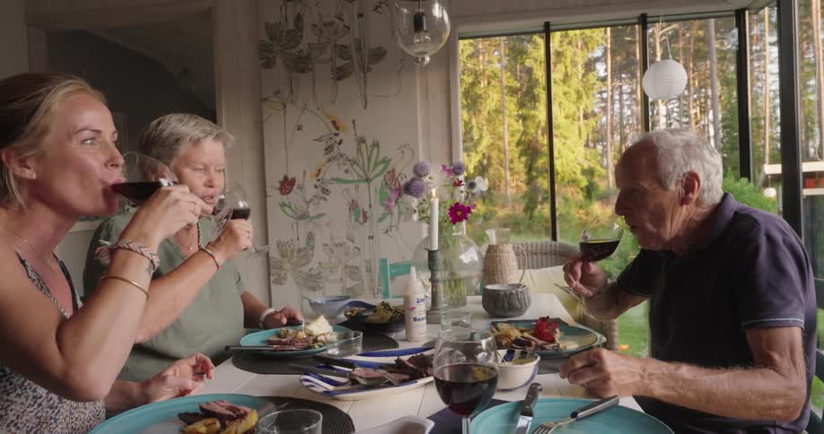 A family seated around a dining table raise their glasses of red wine in a toast