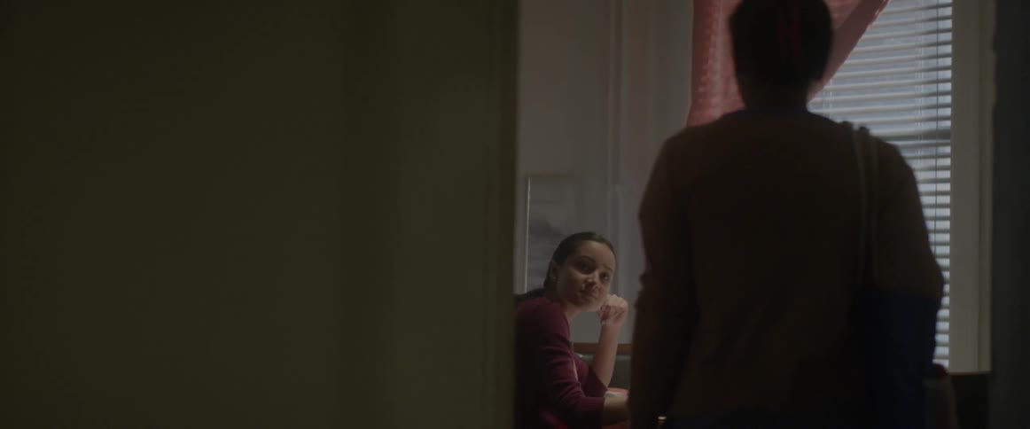 A person walks into a room where a teenage girl is doing her homework and says something to her which makes her sad