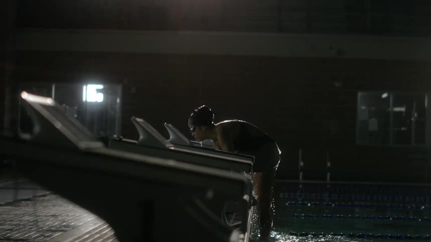 A swimmer emerges from a dimly lit pool dripping water