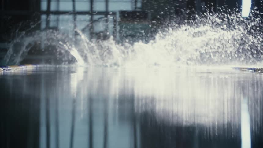 A swimmer poised on a starting block at the edge of a pool jumps in and dives