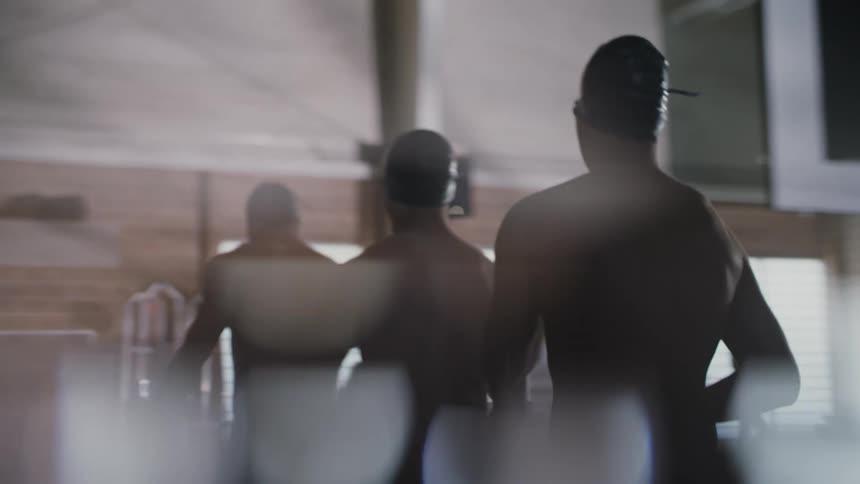 Swim team members stretch while walking across a natatorium