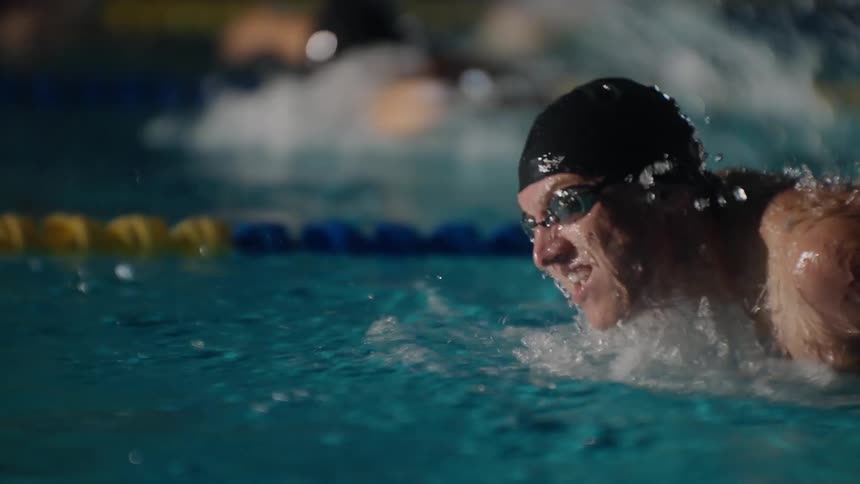 A swimmer in propels through a pool water splashing around as their arm cuts through the water