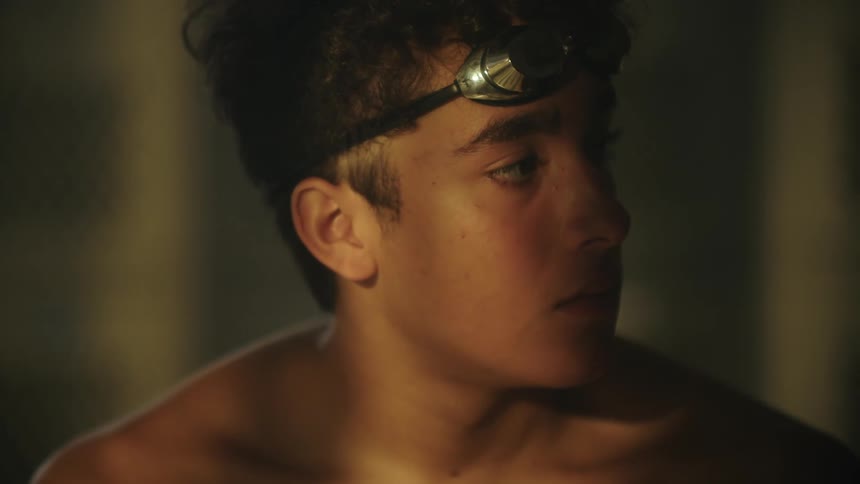 Portrait of a shirtless boy sitting with swimming goggles and reflection of light and shadow on his face