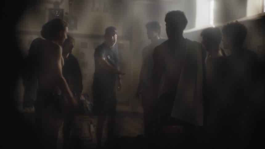 Coachs view of a group of boys joining hands and lifting themselves up in a locker room