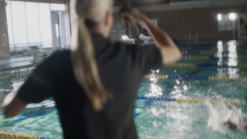 Woman following a group of swimmers swimming in their lanes in a pool and clapping at the end