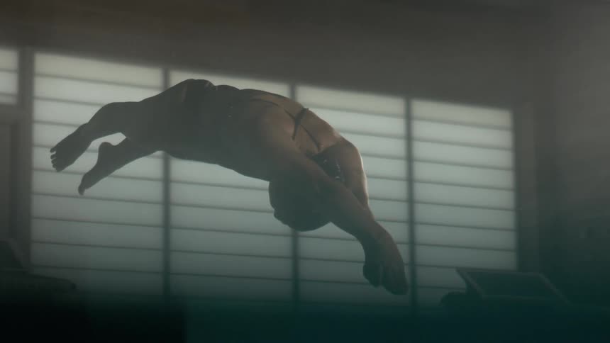 A woman in a swimming costume is diving into the pool water and makes a splash when she hits the water