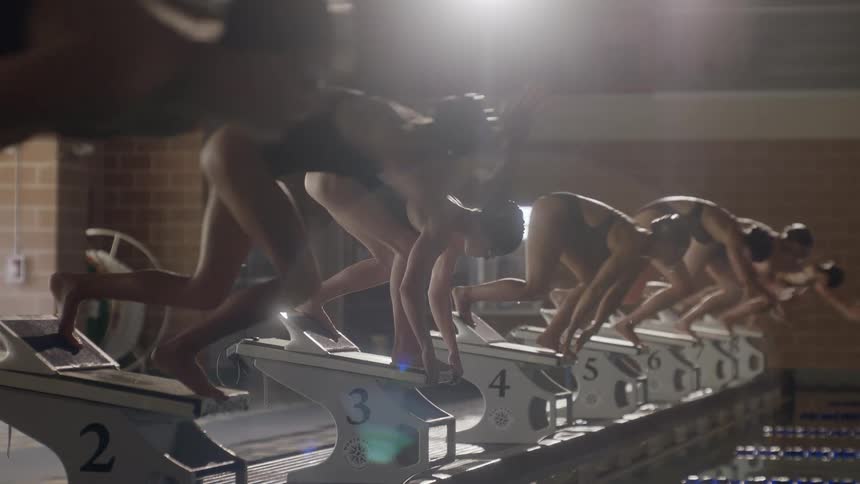Female swimmers in starting position jumping into the pool