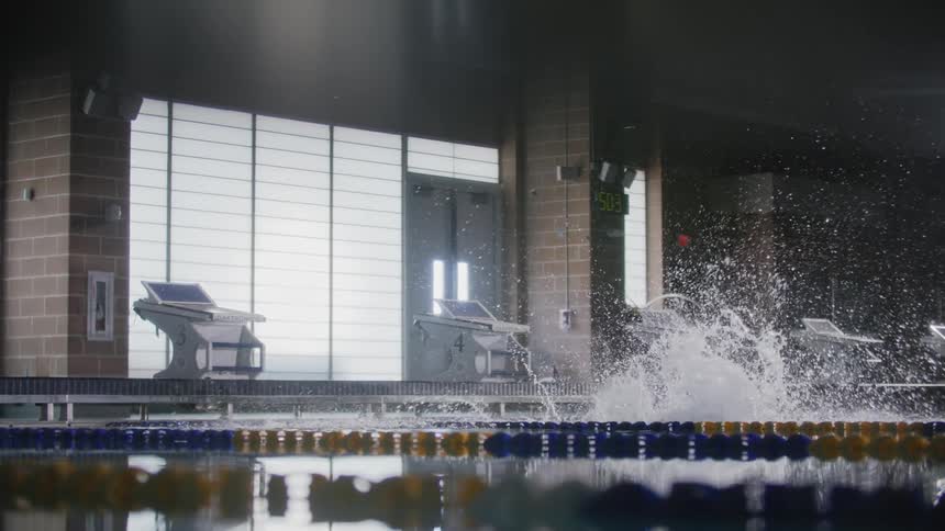 A swimmer poised on a starting block at the edge of a pool jumps in and dives